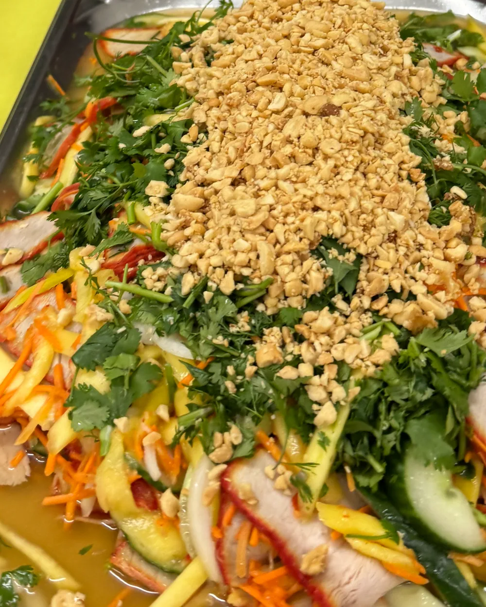 Un grand plat de salade mango à partager : mangue, porc laqué, concombre, carotte, herbes fraîches et cacahuètes concassées.