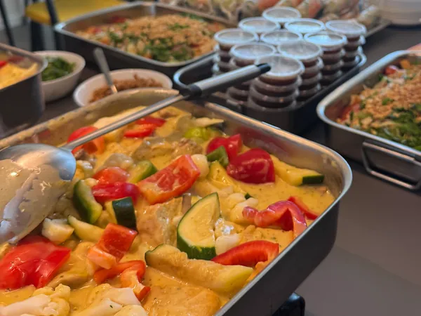 Un buffet installé sur un comptoir de bureau : un bac de curry aux légumes, deux plats de salade aux cacahuètes et des pots de sauce.