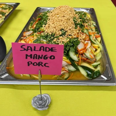 Un plat de salade mango sur la table du buffet, avec son étiquette écrite à la main : salade mango porc.