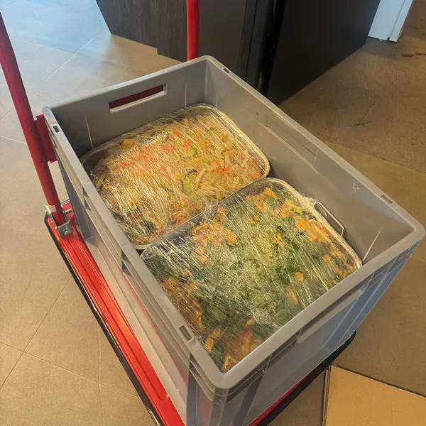 Deux plats sous film alimentaire, dans une caisse, sur un chariot de livraison.