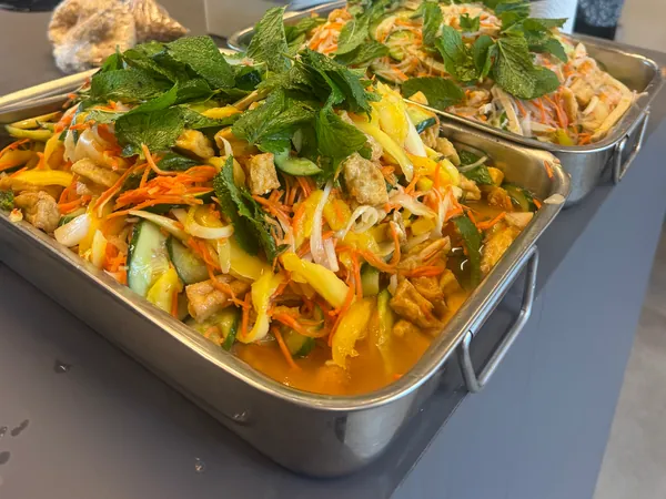 Deux grands plats de salade à partager, garnis de menthe fraîche, posés sur un comptoir de bureau.